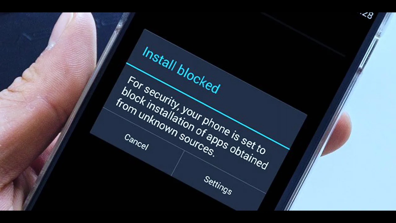 A phone in a hand showing an 'Install blocked' warning about apps from unknown sources